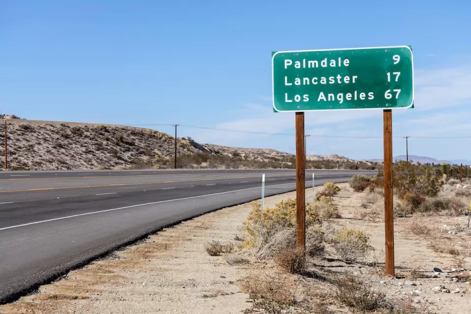 Green highway sign with white text with distances for Palmdale, Lancaster, and Los Angeles, California.